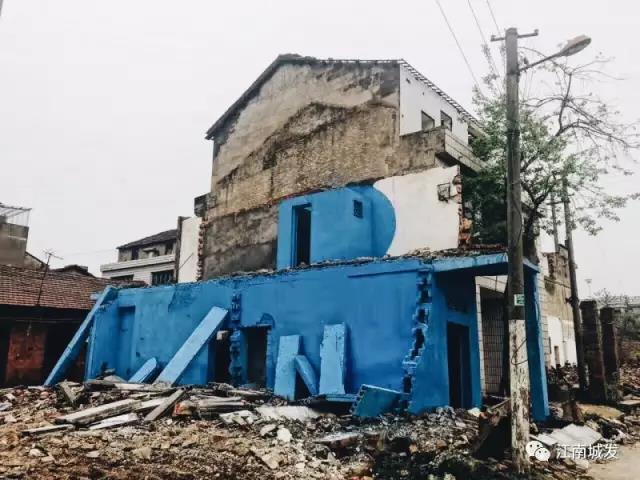 △ 這棟建筑是臨江最近的半拆遷建筑物的遺留，沅江和堤壩成為了展覽的天然背景。創(chuàng)作團隊對這棟建筑進行了半涂裝，將符號性的沅水曲線與拆遷進行中的建筑立面進行意義的疊造，它們共同觸發(fā)了場所空間多元語境的生成，把拆遷這種暫時破壞性、干擾性的介入行動與沅水右岸發(fā)展的未來性、美好性緊密融合。